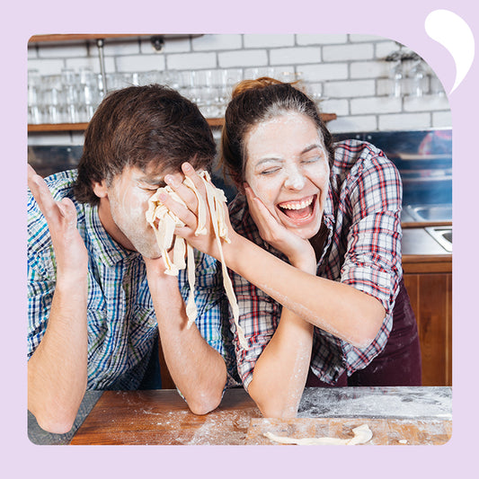 happy woman in a kitchen with flour on her face playfully shoving baking dough into a mans face