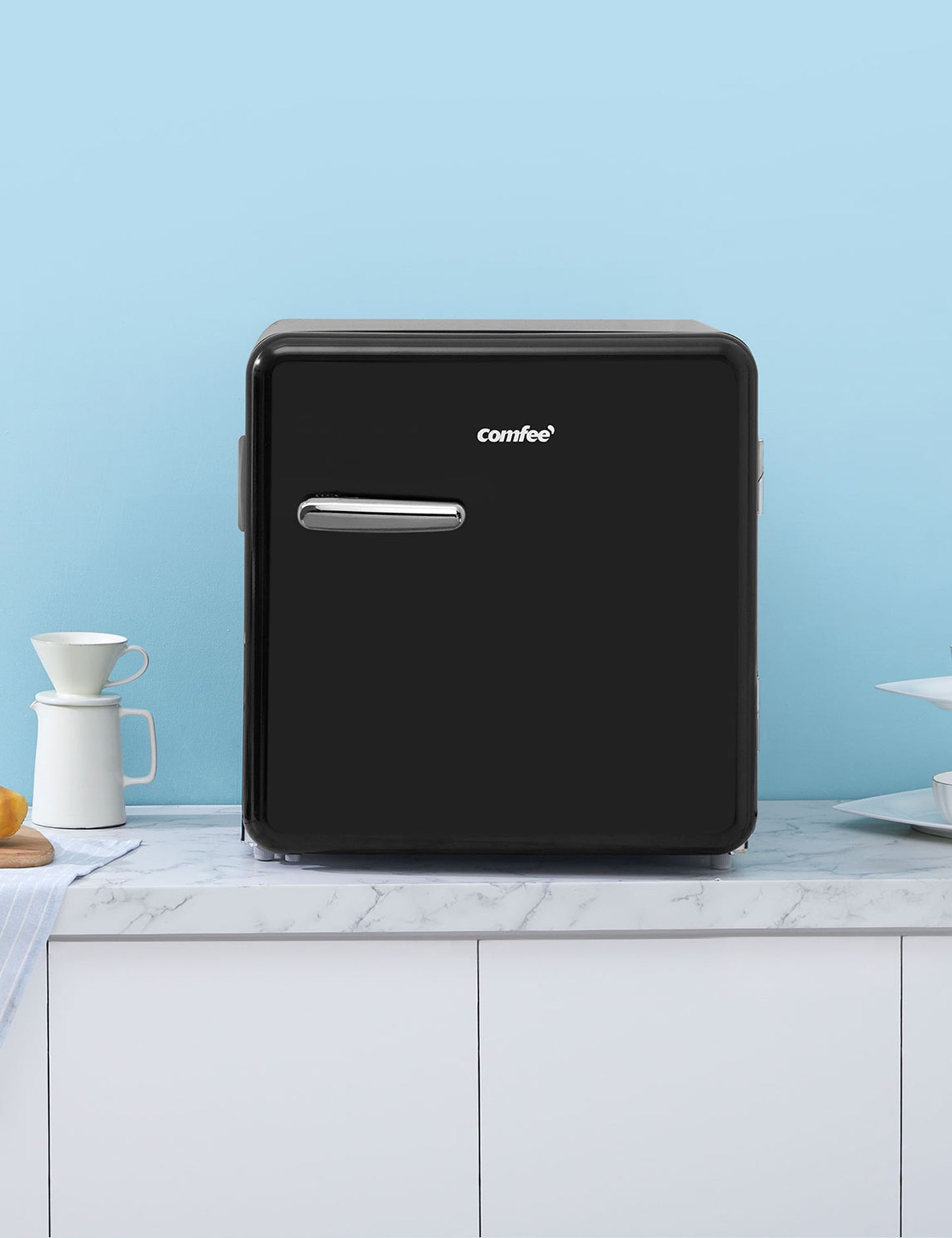 black comfee mini refrigerator on a countertop next to donut and cup