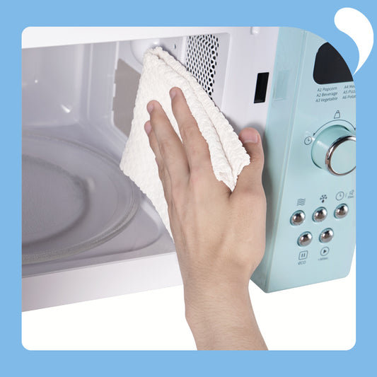 One hand wiping the inside of the microwave oven