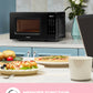 Pizza was baking in a comfee retro microwave on the table, and some baked goods were placed on a table not far away