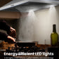 a man cooking food in the dark under a ducted range hood with its led lights on